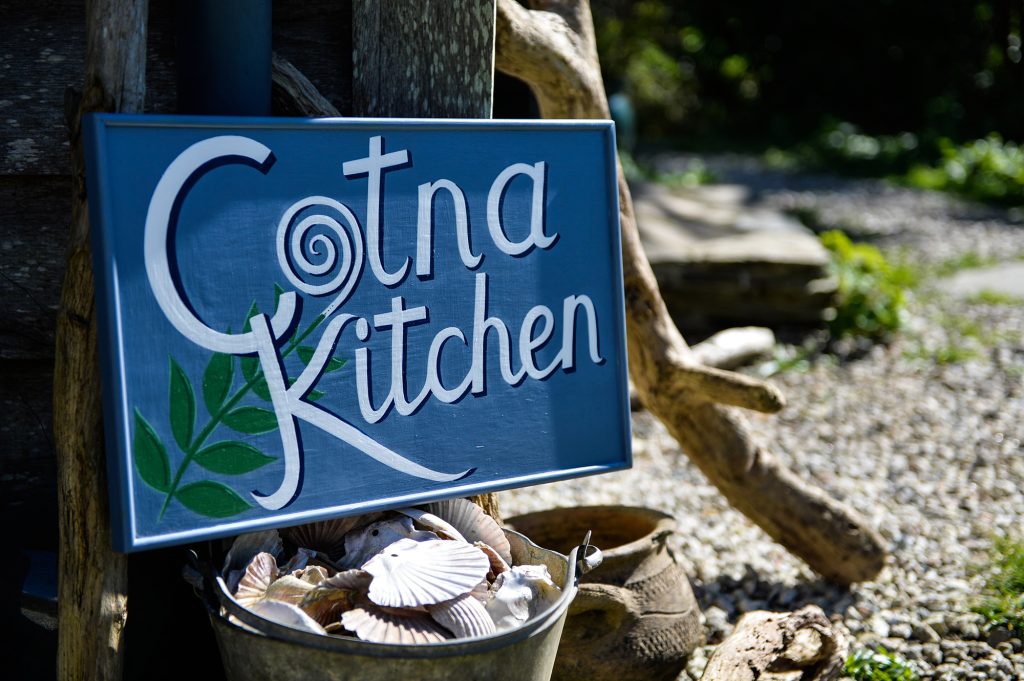 Cotna Kitchen sign at Cotna Eco Retreat, Cornwall, with seashells and beach driftwood. Organic hampers available from the kitchen, also cookery classes in sourdough breadmaking, vegetarian and vegan food