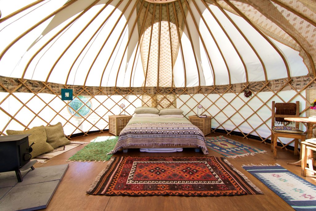 Luxury Gilliflower yurt interior for Cornish glamping holidays with double bed, woodburner, cooking facilities and Turkish rugs with green energy solar lights