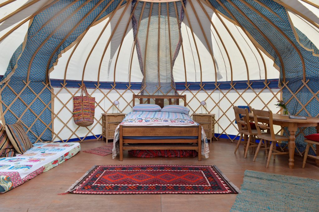 Luxury Tregonna King yurt interior for Cornish glamping holidays with double bed, organic seasalt sheets, dining table, green energy solar lights and Turkish rugs