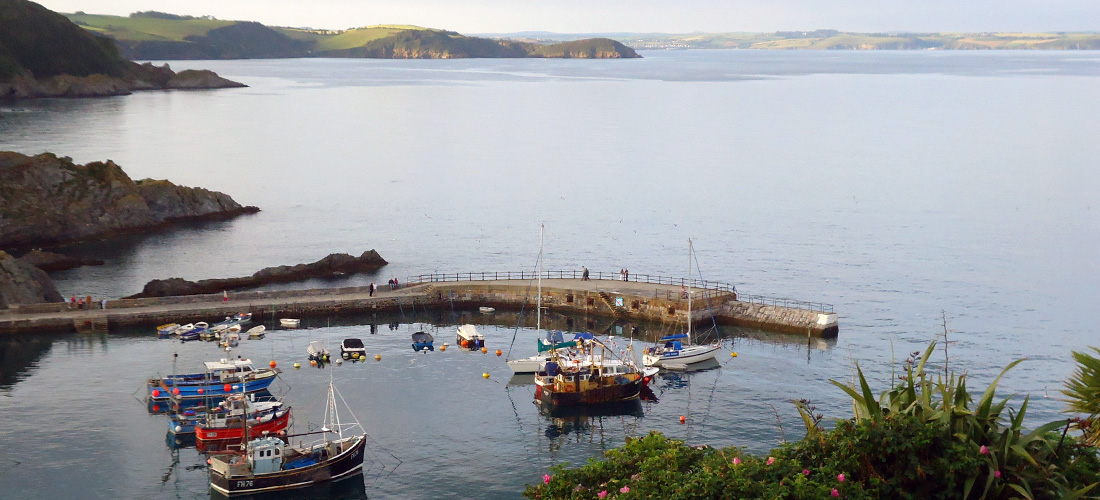 View over Mevagissey harbour on the Roseland. Fishing boats, calm sea, coastline looking towards Fowey