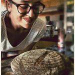 Sourdough Bread made Easy Courses. Sourdough bread course taught by Sara at Cotna Eco Retreat near Mevagissey, South Cornwall. Image shows a guest smiling as she smells her freshly baked sourdough loaf in Cotna Kitchen